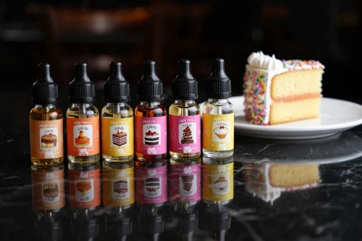 A selection of dessert-themed e-liquid bottles next to a slice of cake, showcasing some of the best vape flavours.